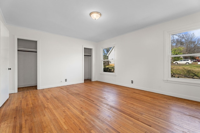 unfurnished bedroom featuring baseboards, light wood-style floors, and multiple closets