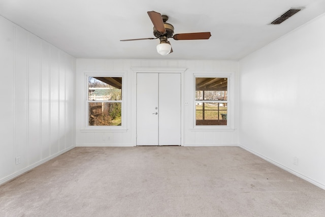 unfurnished bedroom featuring ceiling fan, multiple windows, visible vents, and light colored carpet