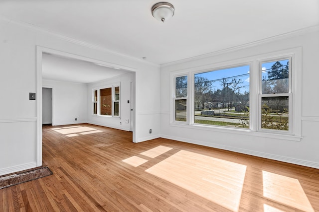 unfurnished room with baseboards, wood finished floors, a wealth of natural light, and crown molding