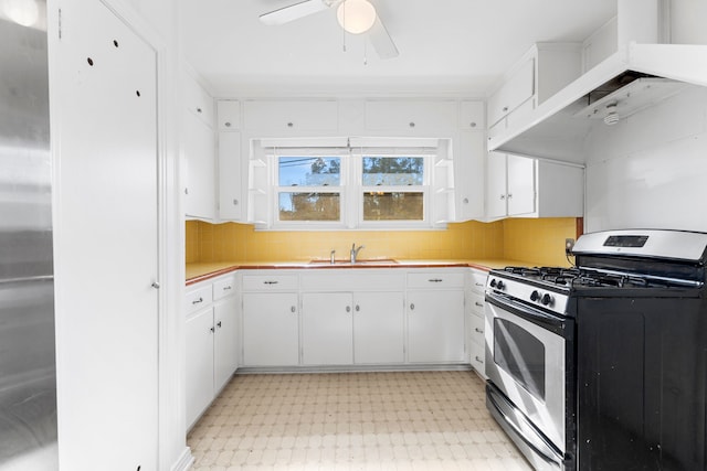 kitchen featuring white cabinets, wall chimney exhaust hood, stainless steel gas range oven, and light countertops