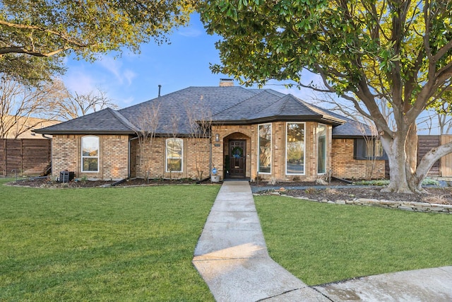 view of front of house with a chimney, roof with shingles, fence, a front lawn, and brick siding