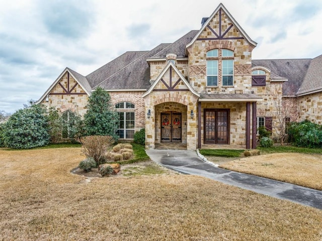 view of front of house with stone siding, a front yard, french doors, and a shingled roof