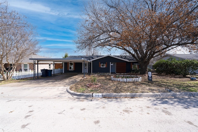 ranch-style home featuring concrete driveway, a carport, and fence