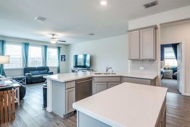 kitchen featuring open floor plan, gray cabinets, light countertops, stainless steel dishwasher, and a sink