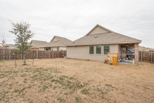 rear view of house featuring a patio area, a fenced backyard, a lawn, and roof with shingles