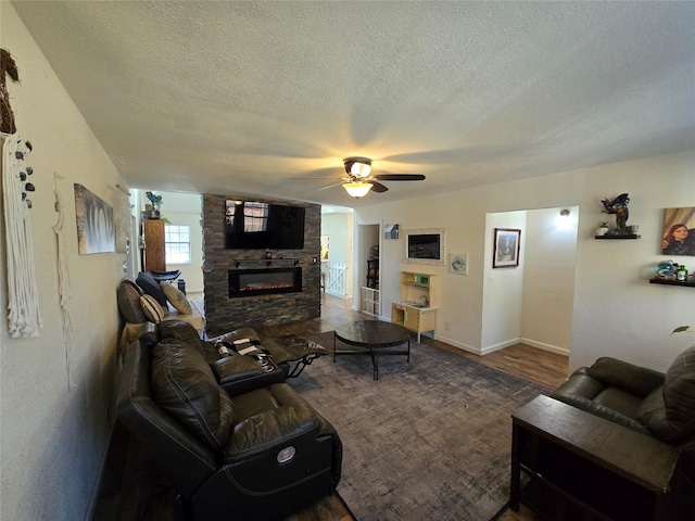 living room with ceiling fan, wood finished floors, a textured ceiling, and a stone fireplace