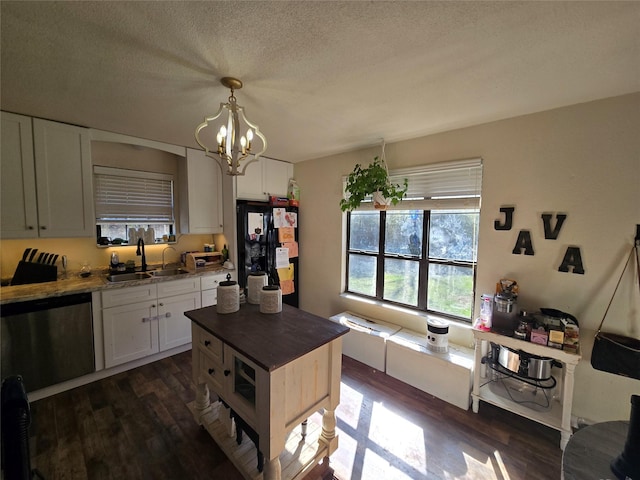 kitchen featuring dark wood-style floors, decorative light fixtures, stainless steel dishwasher, white cabinetry, and a sink