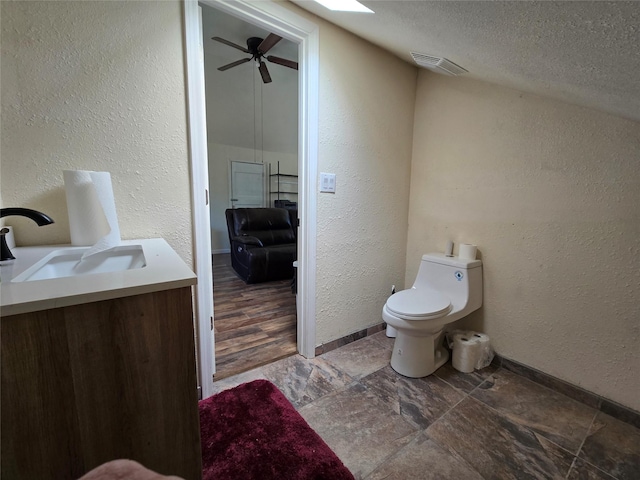 bathroom with a textured ceiling, a textured wall, a ceiling fan, vanity, and stone finish flooring