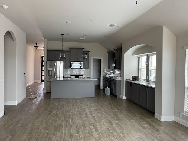 kitchen featuring arched walkways, appliances with stainless steel finishes, a center island, light countertops, and pendant lighting