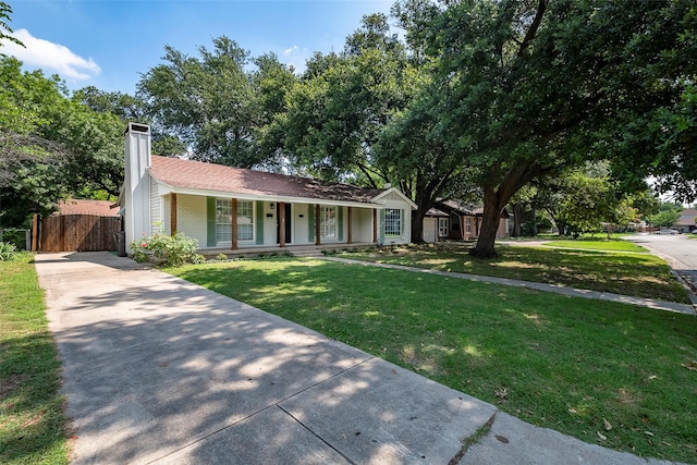 ranch-style home featuring brick siding, a chimney, a porch, a front yard, and driveway