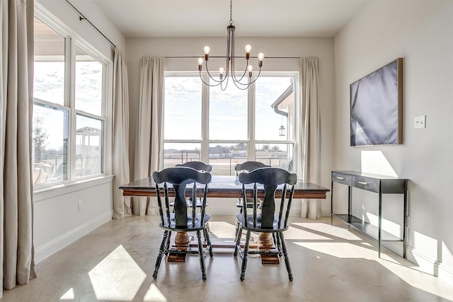 dining area with finished concrete floors, plenty of natural light, baseboards, and an inviting chandelier