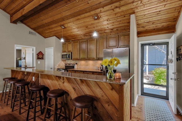 kitchen featuring lofted ceiling with beams, stainless steel appliances, brown cabinetry, and visible vents