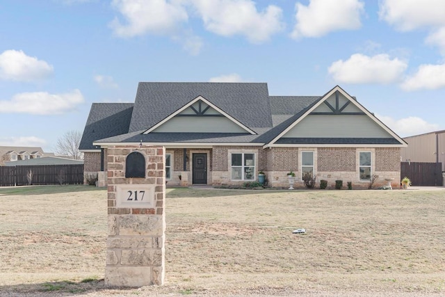 view of front of home featuring a front yard, brick siding, fence, and roof with shingles