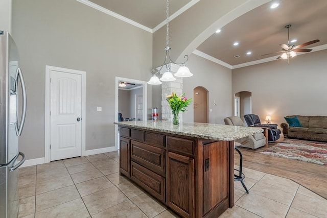 kitchen with light tile patterned floors, arched walkways, crown molding, and freestanding refrigerator