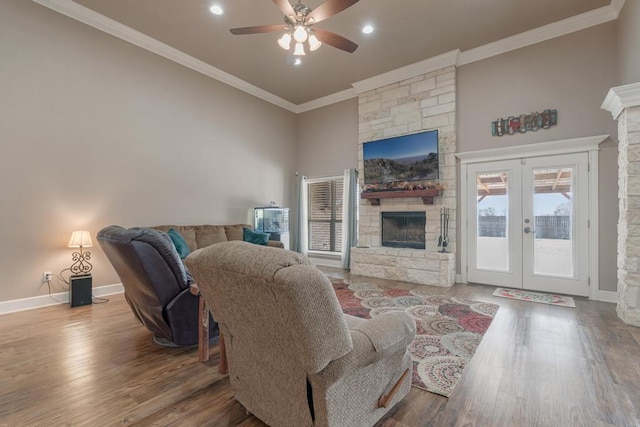 living area with baseboards, ornamental molding, wood finished floors, a stone fireplace, and french doors