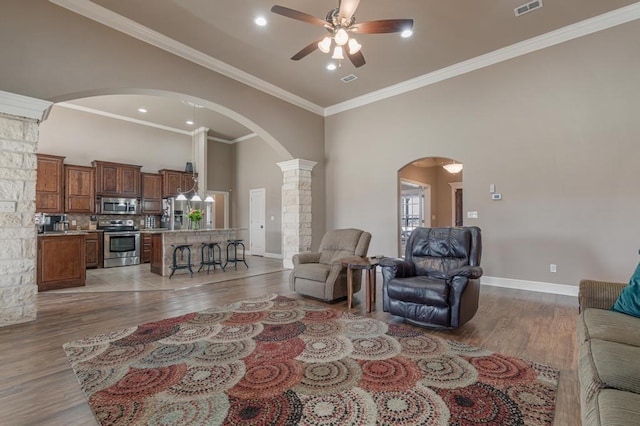 living area with baseboards, arched walkways, ornamental molding, a high ceiling, and light wood-type flooring