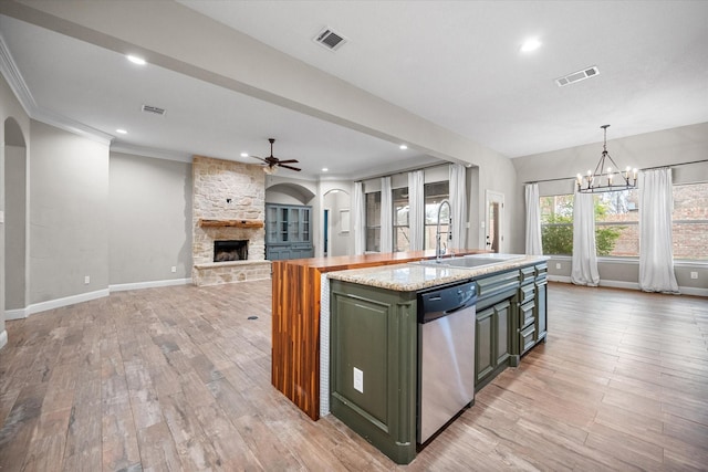 kitchen with a stone fireplace, visible vents, stainless steel dishwasher, a sink, and ceiling fan with notable chandelier