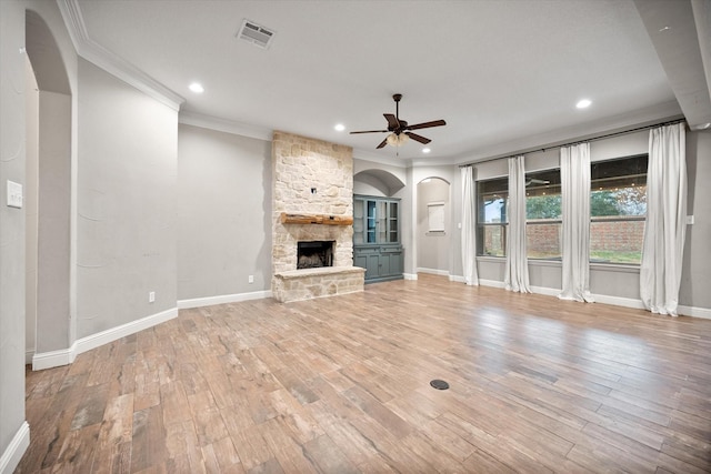 unfurnished living room featuring a stone fireplace, visible vents, a ceiling fan, ornamental molding, and arched walkways