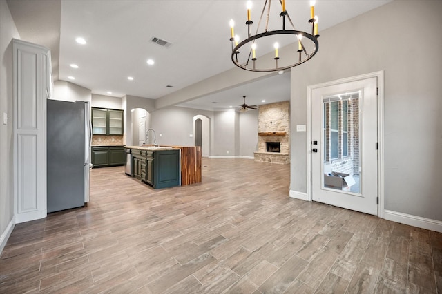 kitchen with arched walkways, open floor plan, visible vents, freestanding refrigerator, and a large fireplace