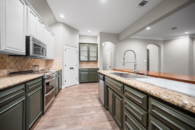 kitchen featuring visible vents, a sink, arched walkways, tasteful backsplash, and appliances with stainless steel finishes