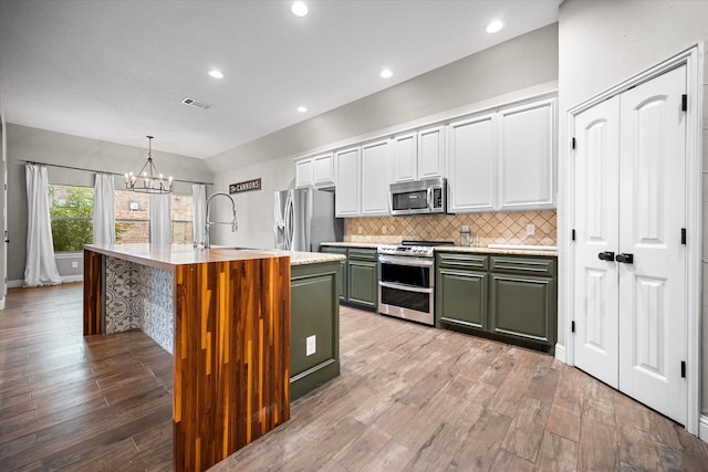 kitchen with stainless steel appliances, a sink, visible vents, light wood-style floors, and green cabinets
