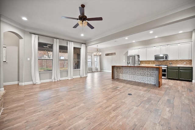 unfurnished living room featuring arched walkways, ceiling fan with notable chandelier, light wood-style floors, and ornamental molding