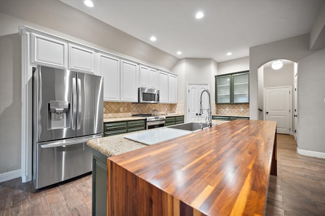 kitchen featuring arched walkways, a sink, baseboards, wooden counters, and appliances with stainless steel finishes