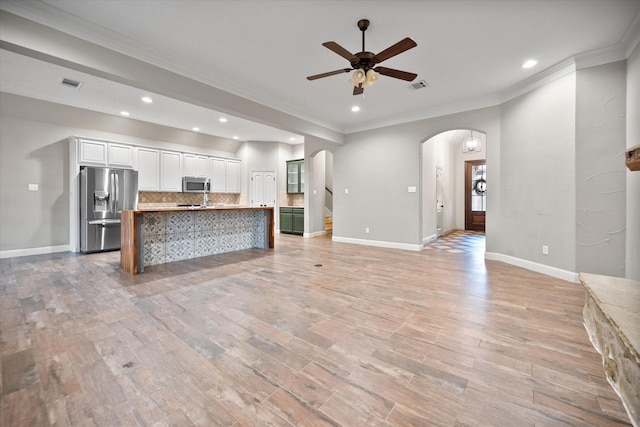 unfurnished living room featuring visible vents, arched walkways, ceiling fan, and crown molding