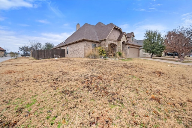 view of front of house with roof with shingles, a chimney, fence, brick siding, and an attached garage