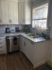 kitchen featuring tasteful backsplash, light countertops, stainless steel dishwasher, white cabinetry, and a sink