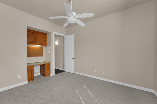 unfurnished bedroom featuring light carpet, baseboards, a ceiling fan, and built in study area