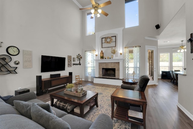 living room featuring a fireplace with raised hearth, ornamental molding, wood finished floors, and a ceiling fan