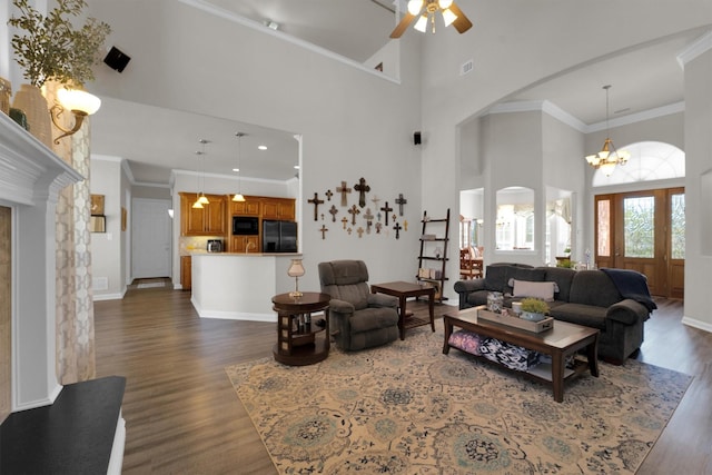 living room with dark wood-style floors, arched walkways, crown molding, and ceiling fan with notable chandelier