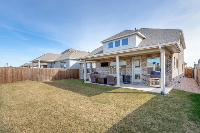 back of property featuring a lawn, a fenced backyard, roof with shingles, a patio area, and brick siding