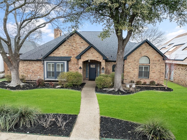 view of front of house featuring a front yard, brick siding, a chimney, and roof with shingles