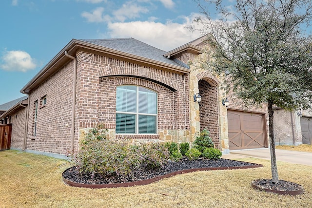 french country home with driveway, a shingled roof, stone siding, a front lawn, and brick siding