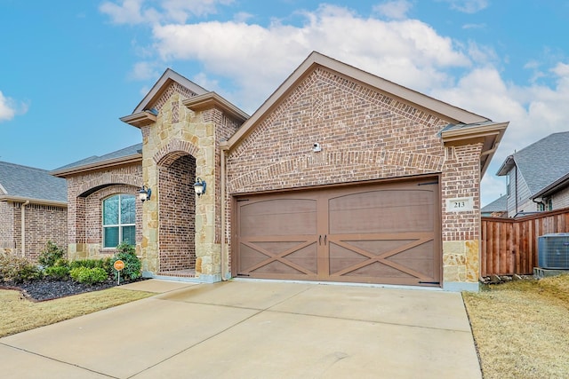 french country style house featuring central AC unit, an attached garage, brick siding, concrete driveway, and stone siding