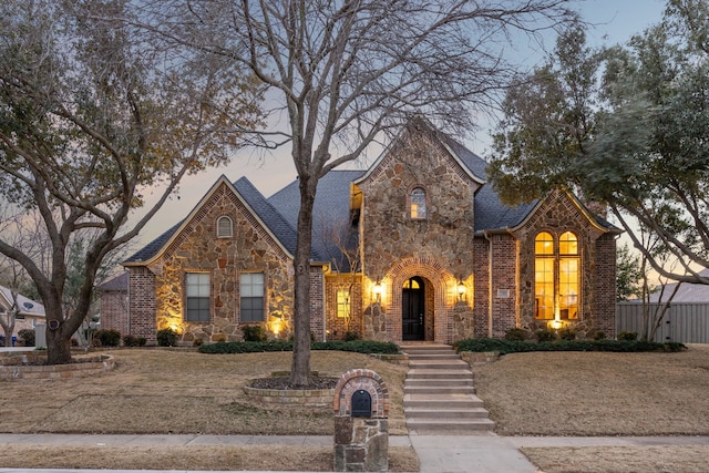 view of front of property featuring stone siding, brick siding, and roof with shingles