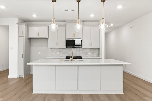 723 Prosper Ln, Wylie, TX 75098 - kitchen featuring stainless steel microwave, light countertops, backsplash, a center island with sink, and light wood-type flooring