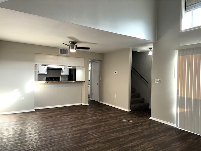 unfurnished living room featuring baseboards, dark wood finished floors, visible vents, ceiling fan, and stairs