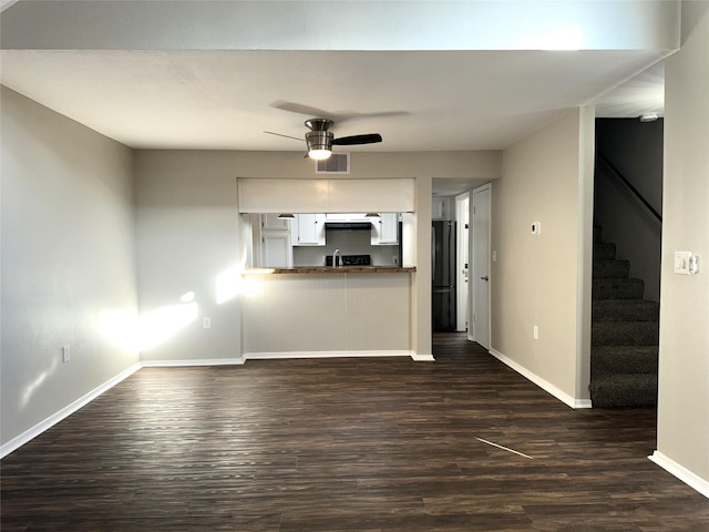 unfurnished living room featuring a ceiling fan, visible vents, stairs, baseboards, and dark wood finished floors