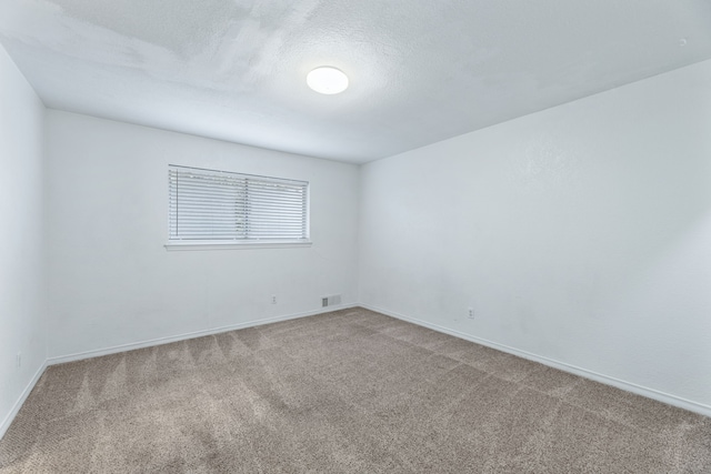 carpeted empty room with a textured ceiling, visible vents, and baseboards