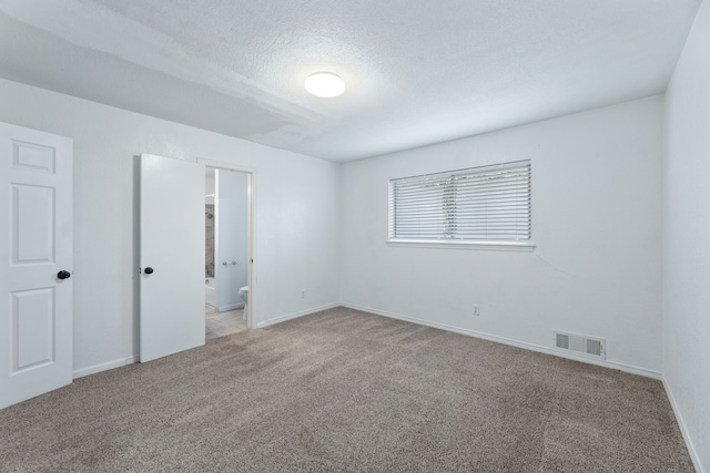 empty room with light colored carpet, visible vents, a textured ceiling, and baseboards