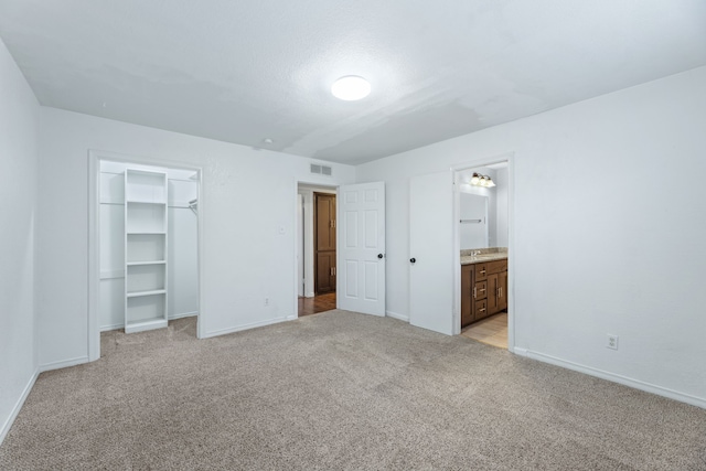 unfurnished bedroom featuring baseboards, visible vents, a walk in closet, and light colored carpet