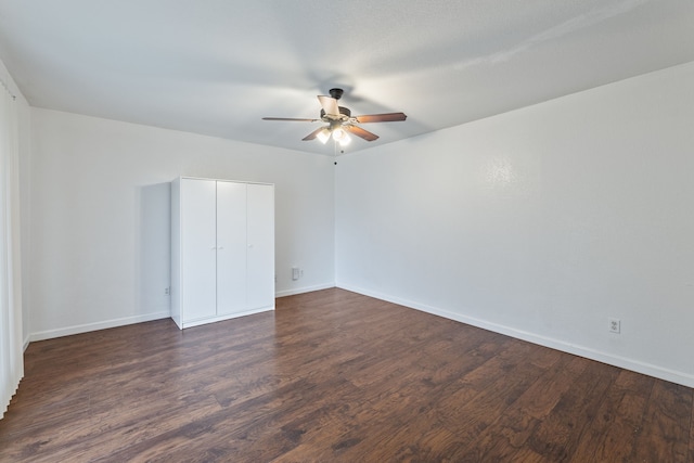 unfurnished bedroom featuring dark wood-type flooring, a closet, ceiling fan, and baseboards