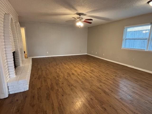 unfurnished living room featuring a textured ceiling, dark wood-style flooring, a fireplace, a ceiling fan, and baseboards