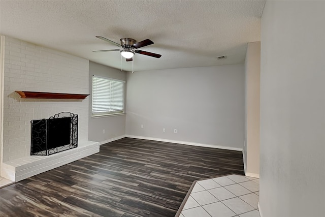 unfurnished living room with a brick fireplace, ceiling fan, baseboards, and wood finished floors