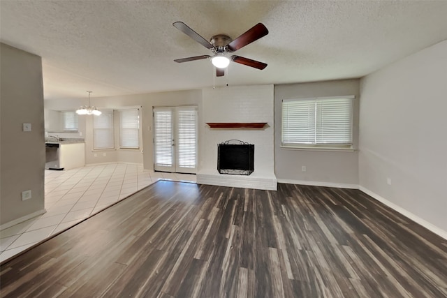 unfurnished living room with a brick fireplace, a textured ceiling, baseboards, and wood finished floors