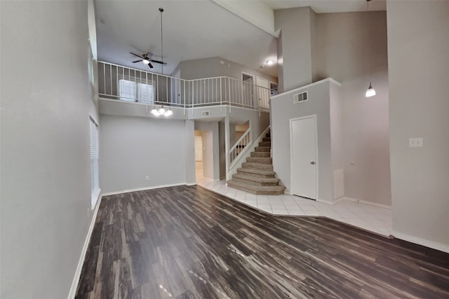 unfurnished living room featuring a high ceiling, wood finished floors, visible vents, baseboards, and stairway