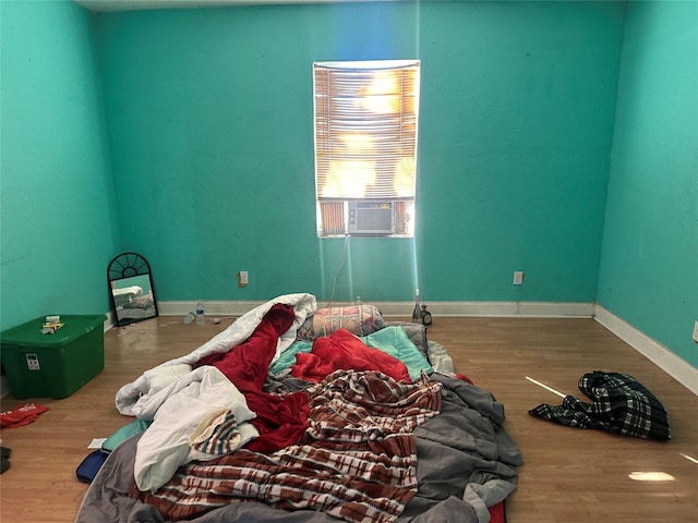 bedroom with cooling unit, baseboards, and wood finished floors